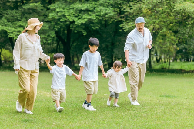 手をつなぎ、緑の中を歩く家族